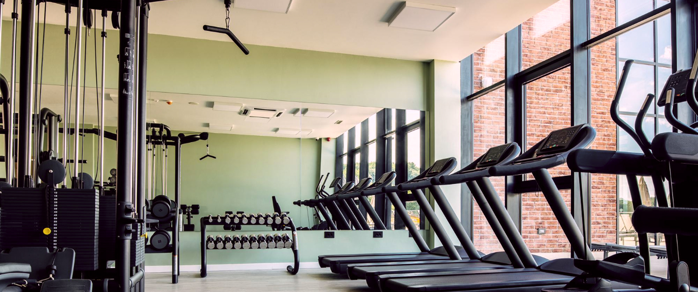 Огромный спортивный зал в теплом цвете, с правой стороны ветражные прозрачные окна и перед ними стоят беговые дорожки, слева стоят различные спортивные тренажеры